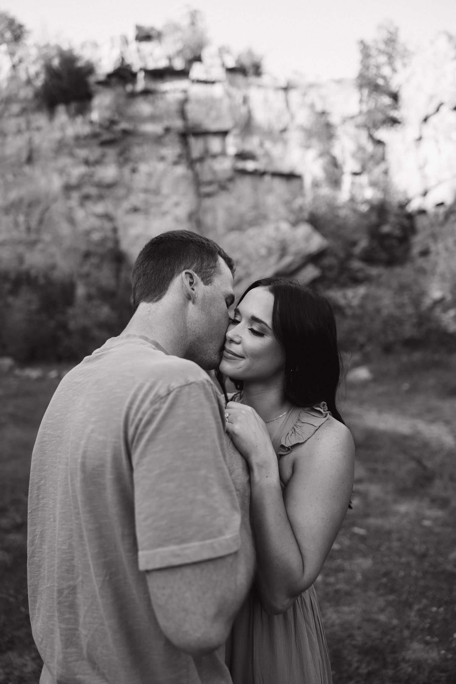Black and white portrait of couple embracing near dramatic rock wall.