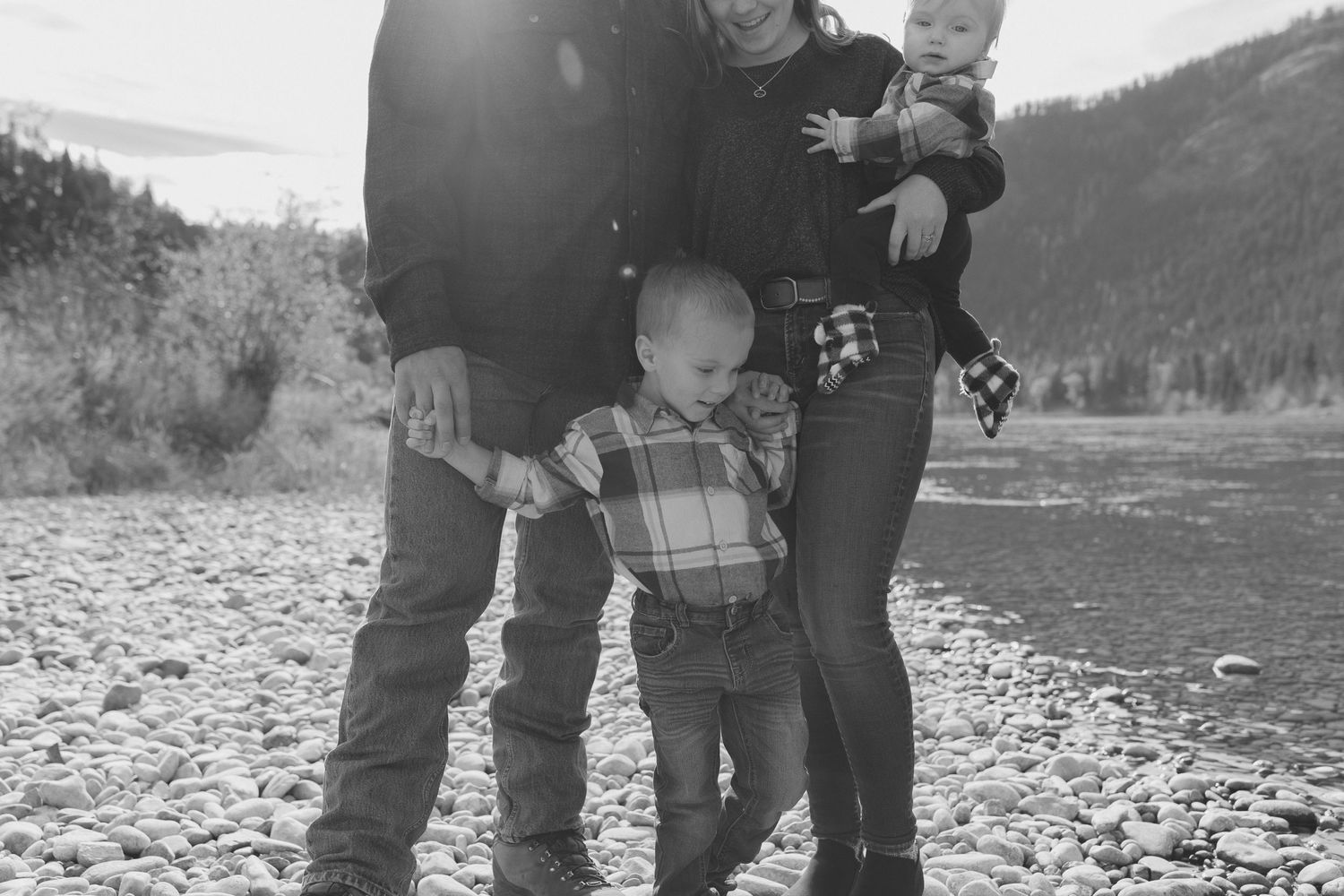 Black and white riverside photo of a family standing on rocky shoreline in winter.