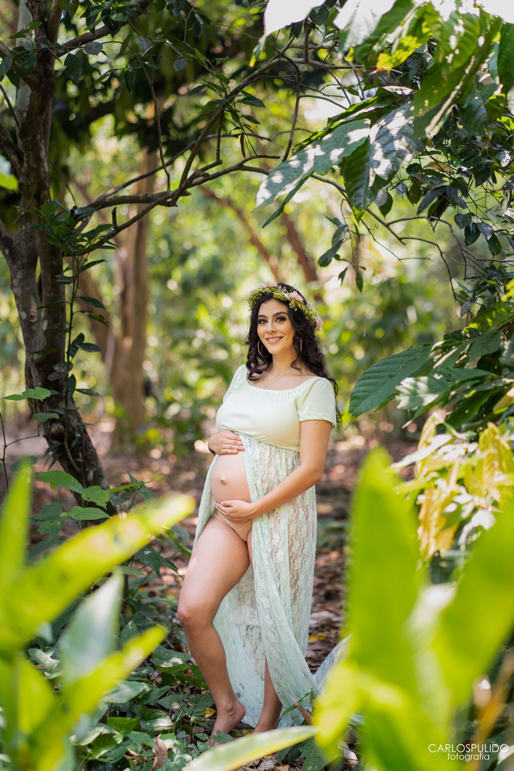 Sunlit garden maternity photo with lush green foliage creating natural framing.