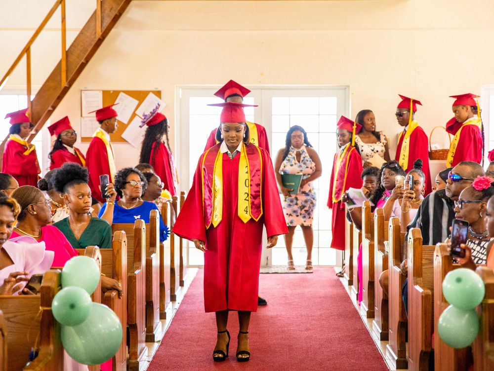Graduate walks down church aisle in red and gold regalia during commencement ceremony.