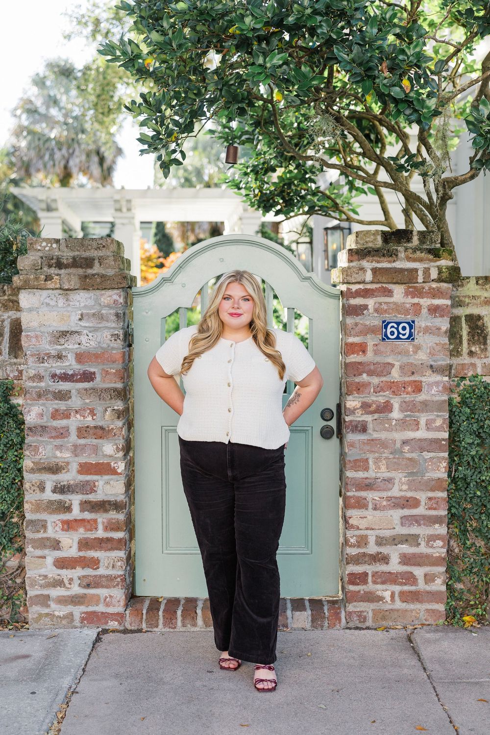 Person poses confidently in front of rustic brick wall and mint green gate.