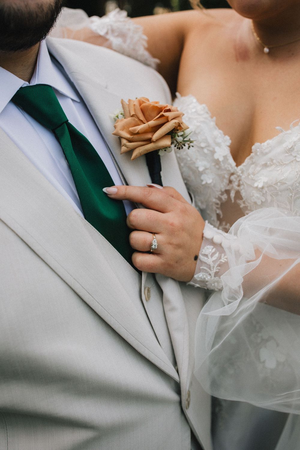 Close-up of peach rose boutonniere on light gray suit with emerald tie and bridal lace details.
