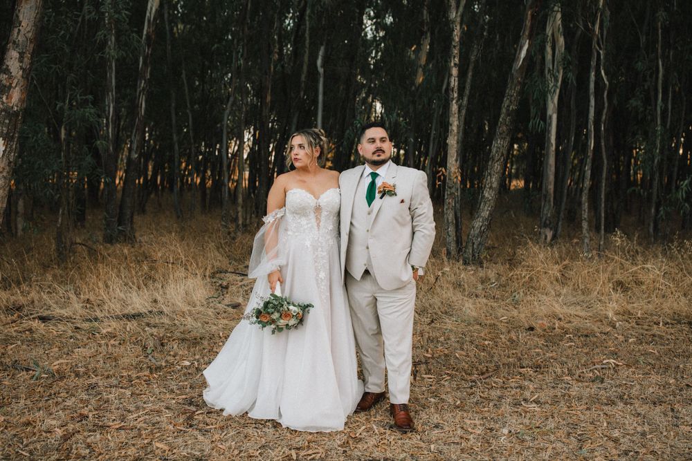 Newlyweds walking together through eucalyptus forest in formal wedding attire.