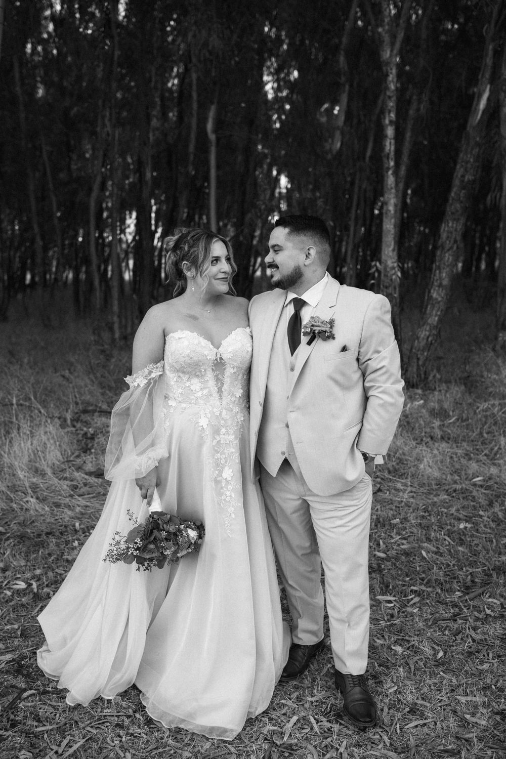 Black and white portrait of newlyweds sharing a joyful moment in a eucalyptus forest.