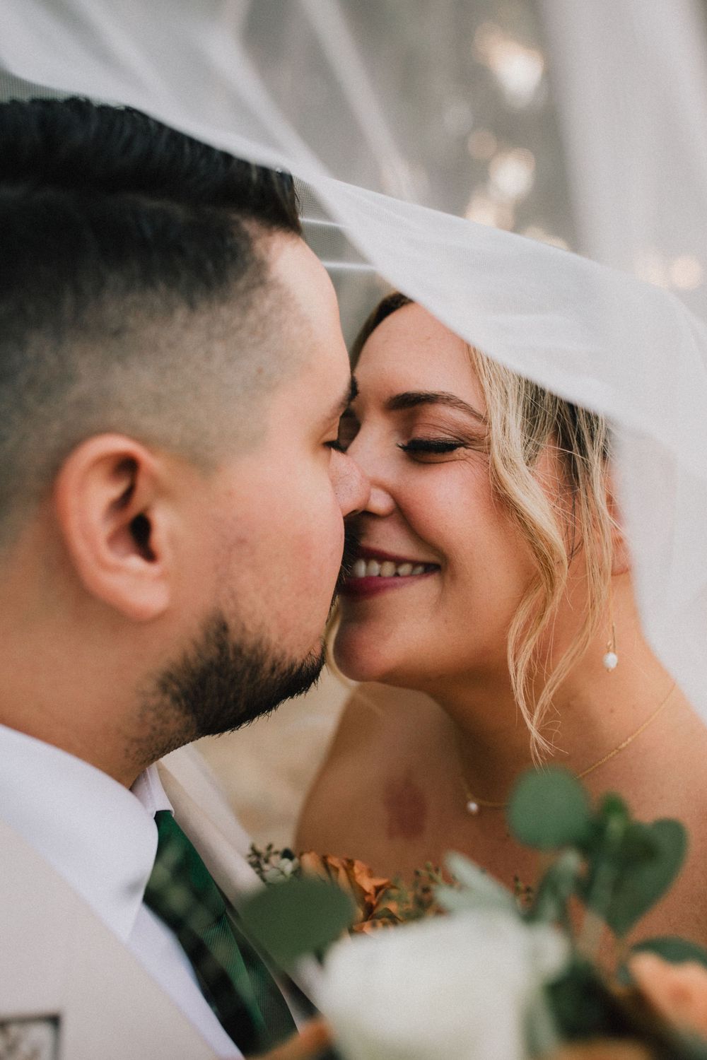 A tender and intimate wedding moment captured as a couple shares a romantic kiss under a delicate veil.
