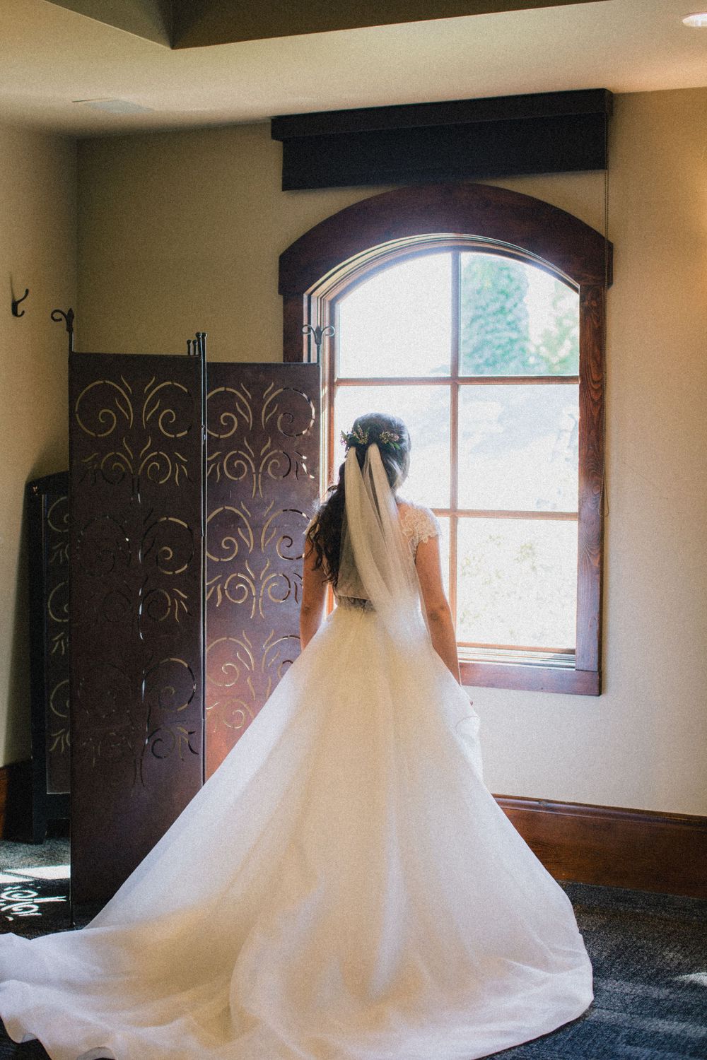 A bride in a ballgown wedding dress gazes out an arched window in dramatic silhouette.