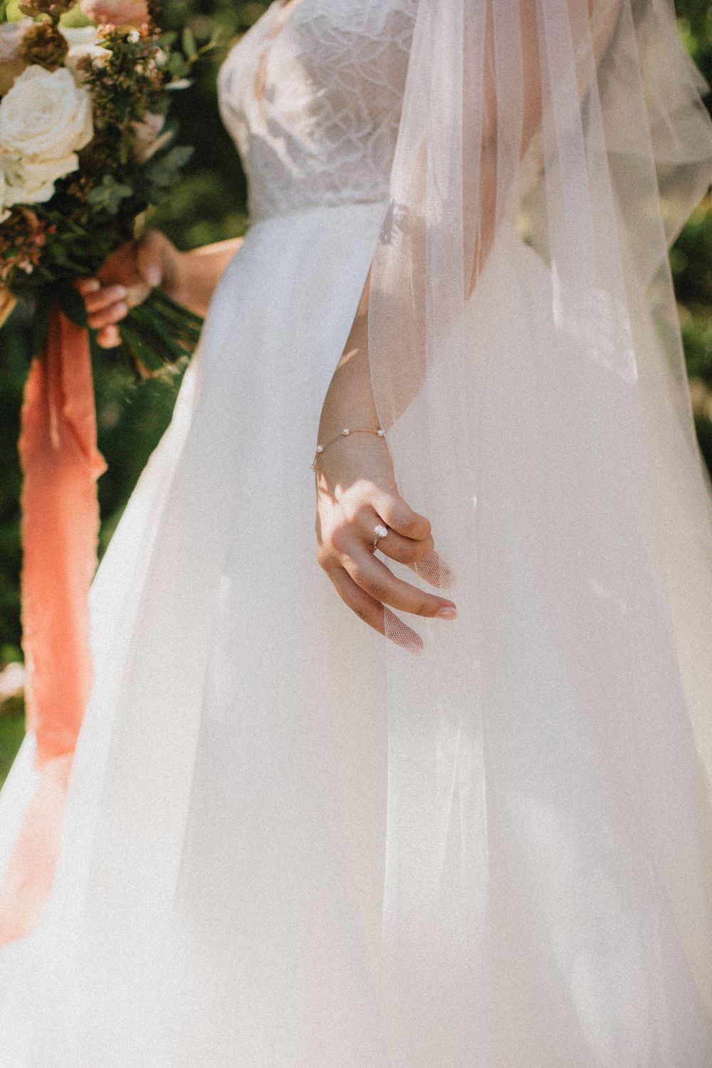 Detail shot of a bride's hand and flowing white wedding dress with delicate lace details.