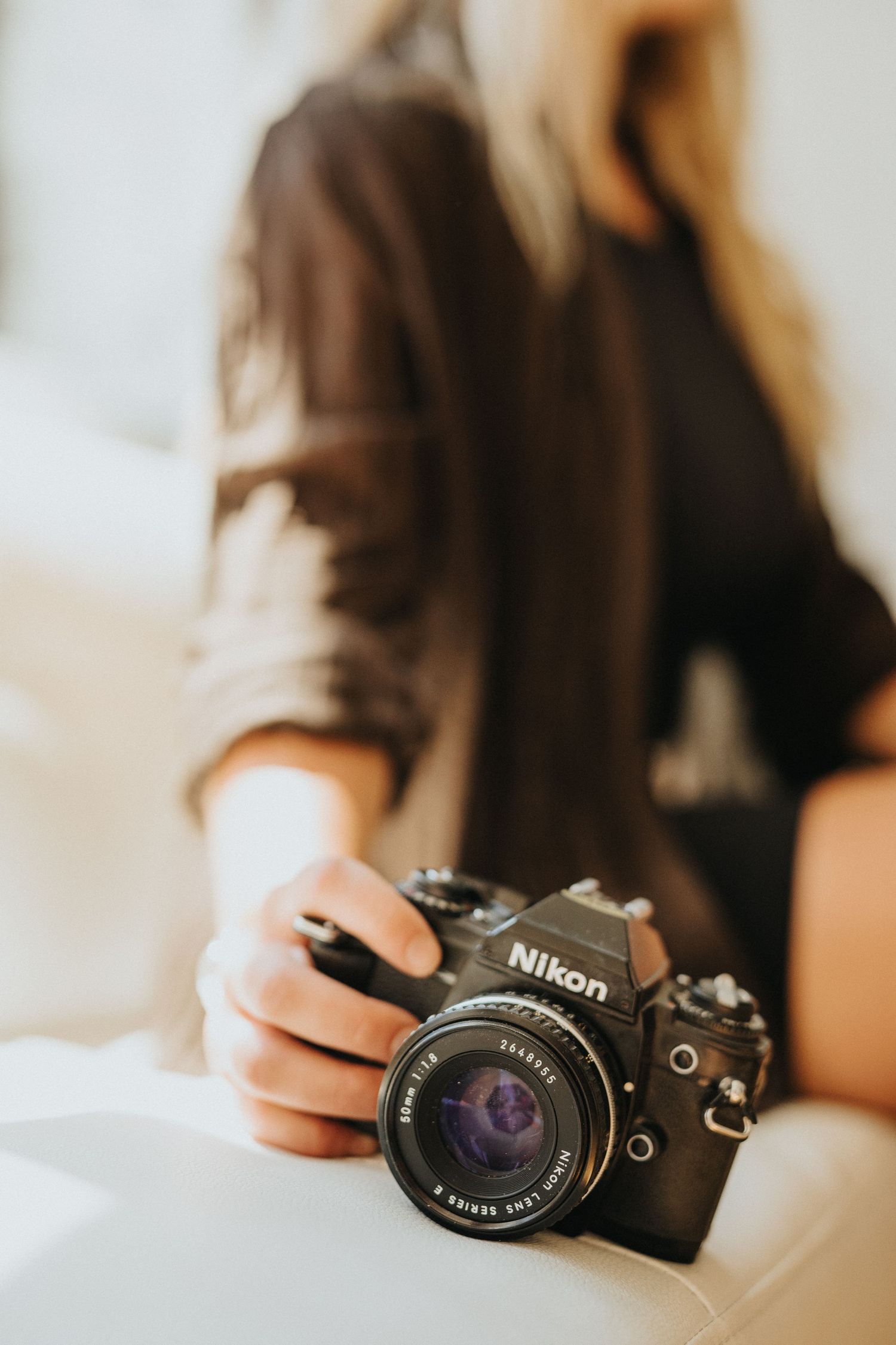 Hands holding a vintage Nikon camera with natural light streaming through a window.