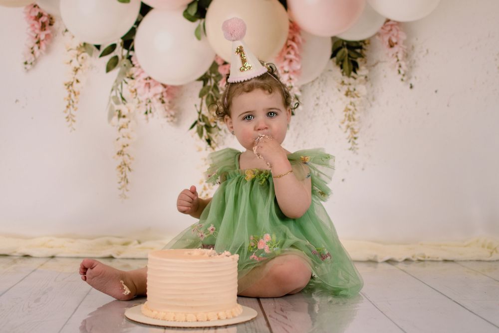 Birthday celebration setup with cake and pink balloons against white wall.