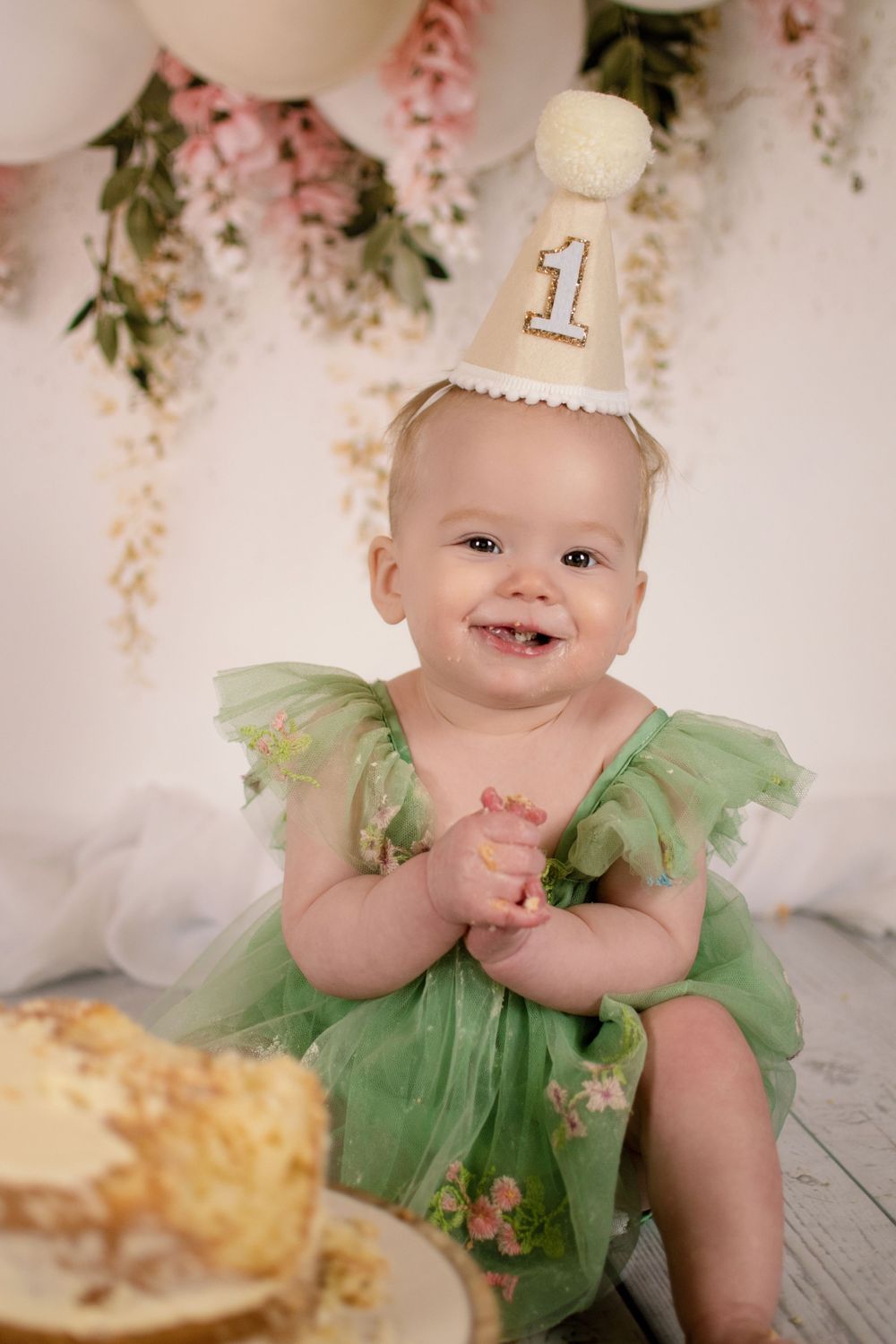 First birthday celebration with green tulle dress and pink floral backdrop.