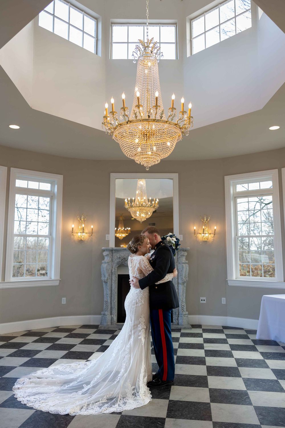 A couple embracing under an elegant crystal chandelier in a room with checkerboard floors.