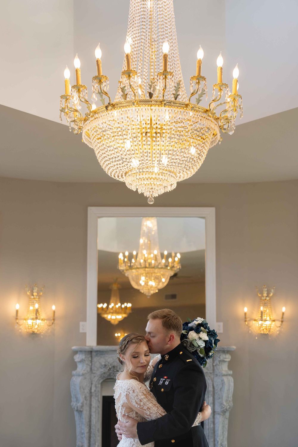 An elegant ballroom wedding scene with a stunning crystal chandelier and ornate fireplace.