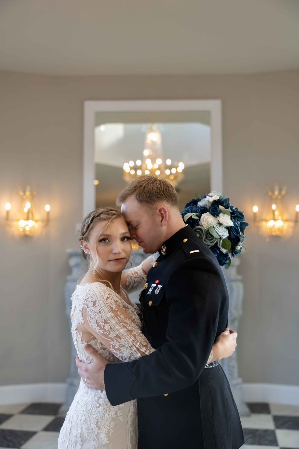An intimate wedding moment captured beneath a crystal chandelier in an elegant ballroom.