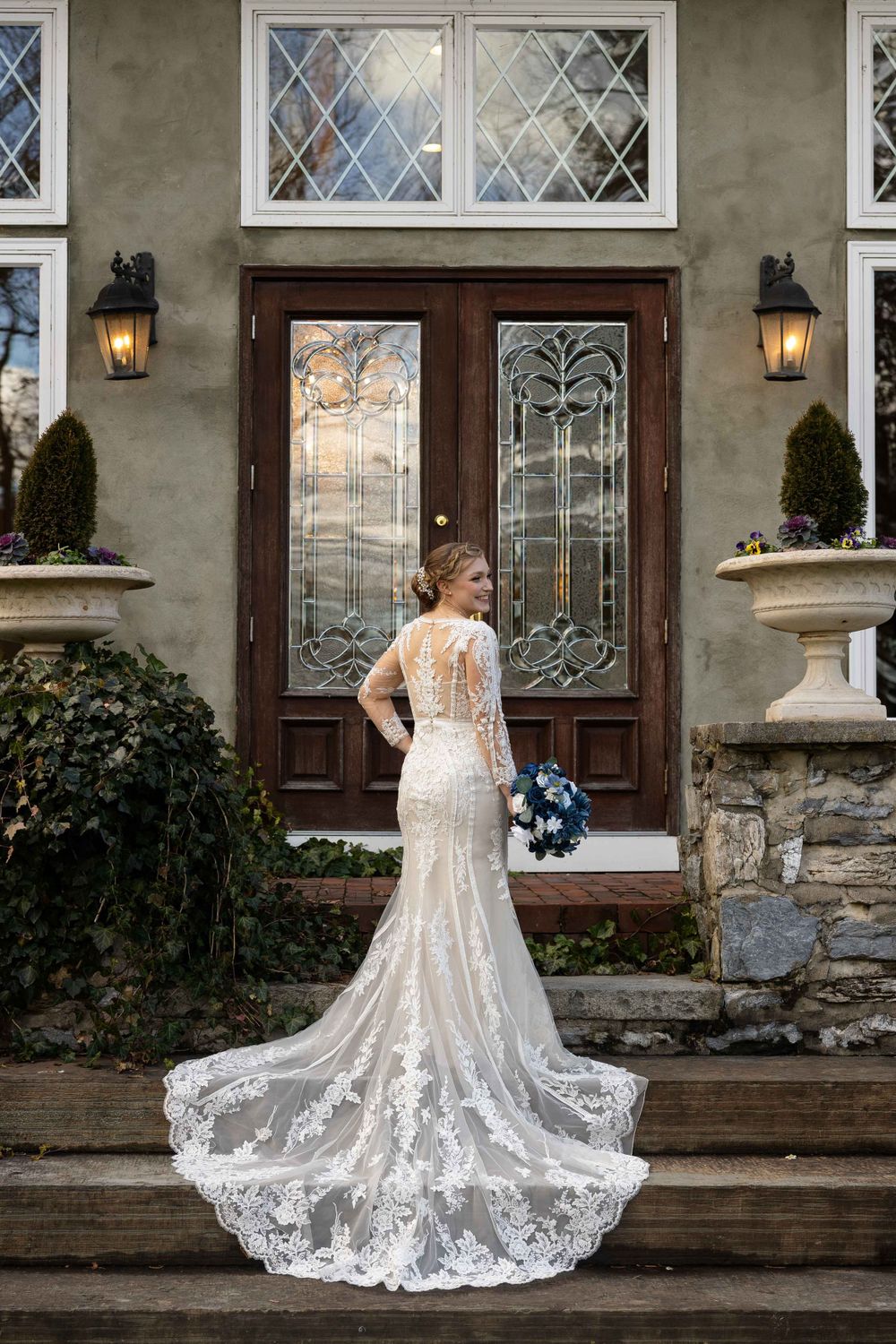 A wedding dress with intricate lace train photographed in front of ornate glass doors.