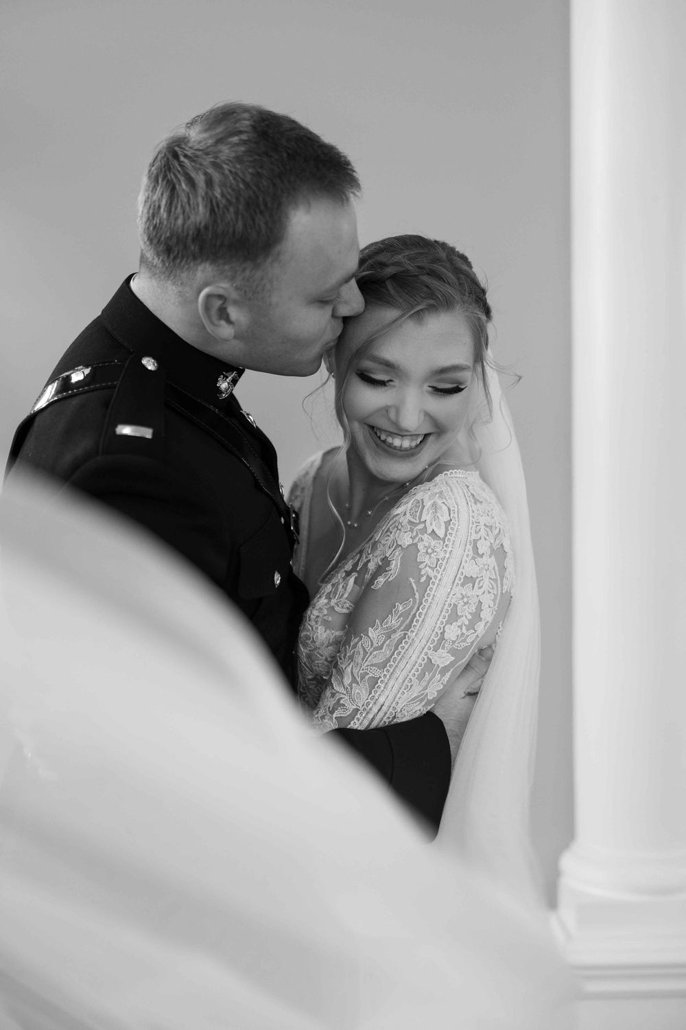 Intimate black and white portrait of newlyweds sharing a tender moment in formal military and wedding attire.