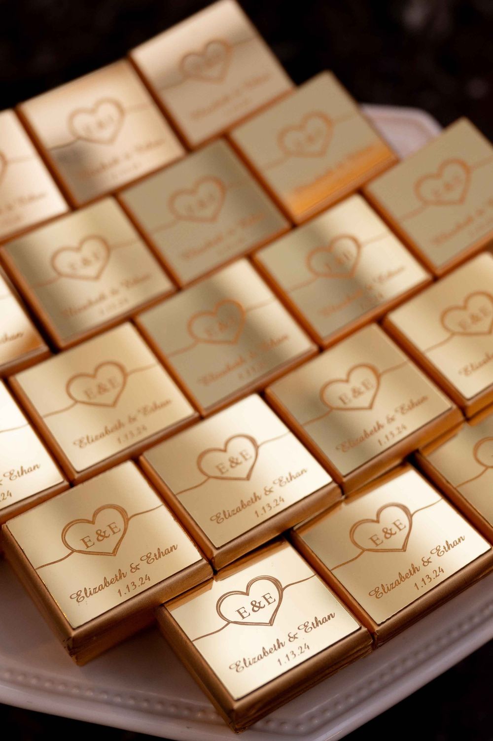 Gold wedding favor boxes arranged in rows featuring embossed hearts and names.