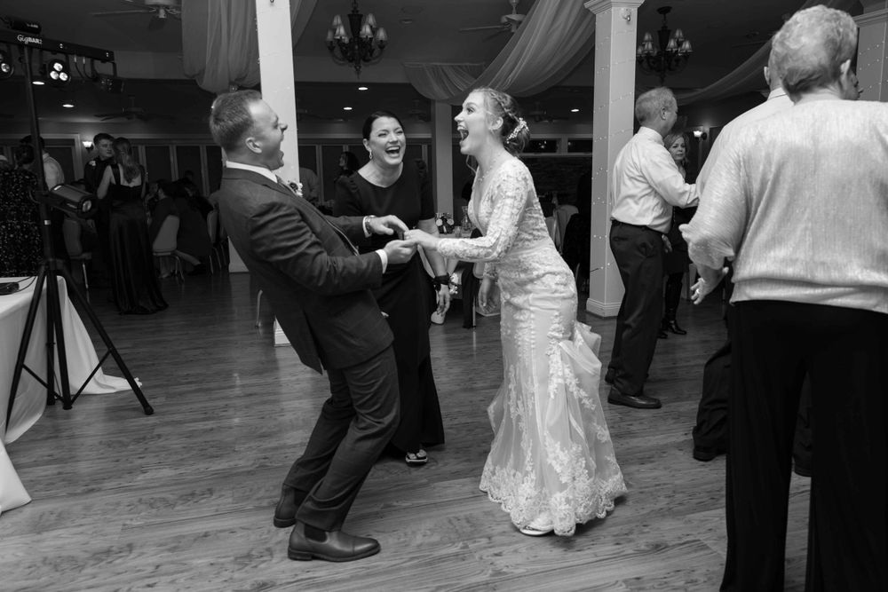 Black and white photo of wedding guests dancing energetically on a wooden dance floor.