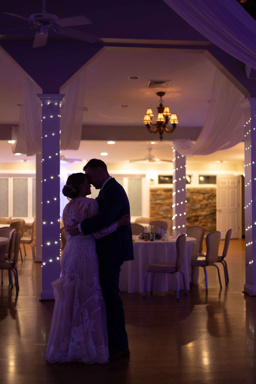 Silhouetted couple sharing an intimate dance under twinkling lights in an elegant reception venue.