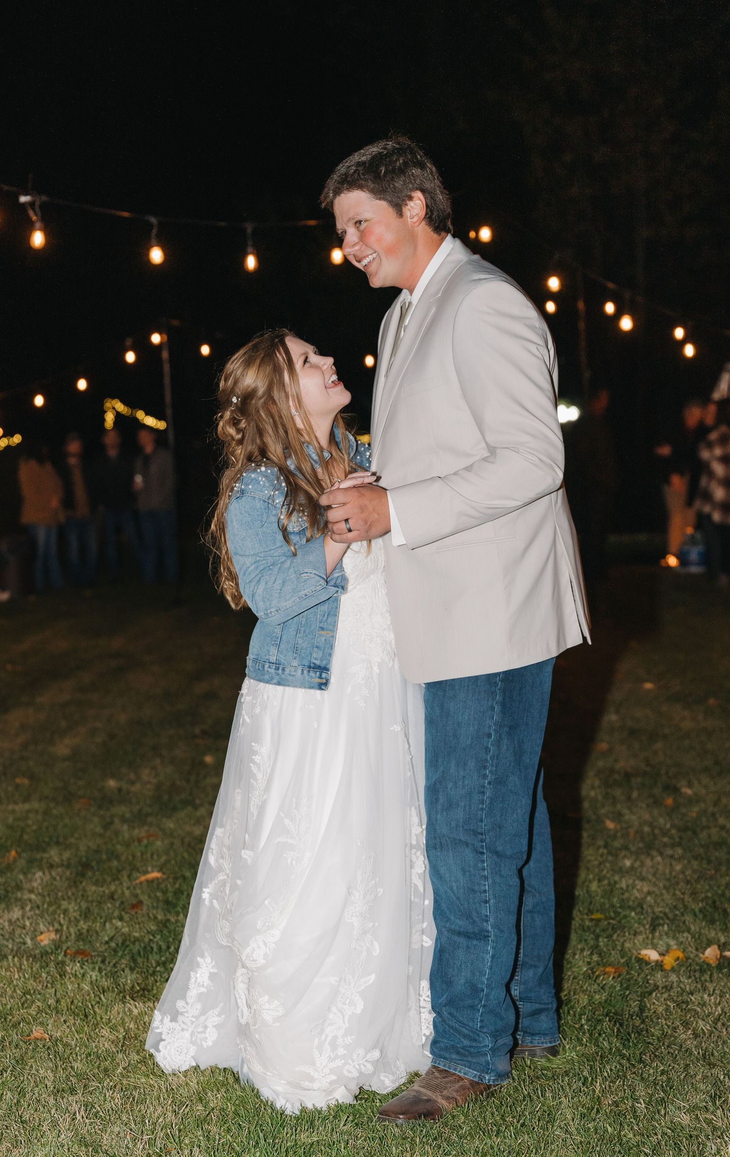 A couple shares a dance moment outdoors at night under string lights on a grassy area.