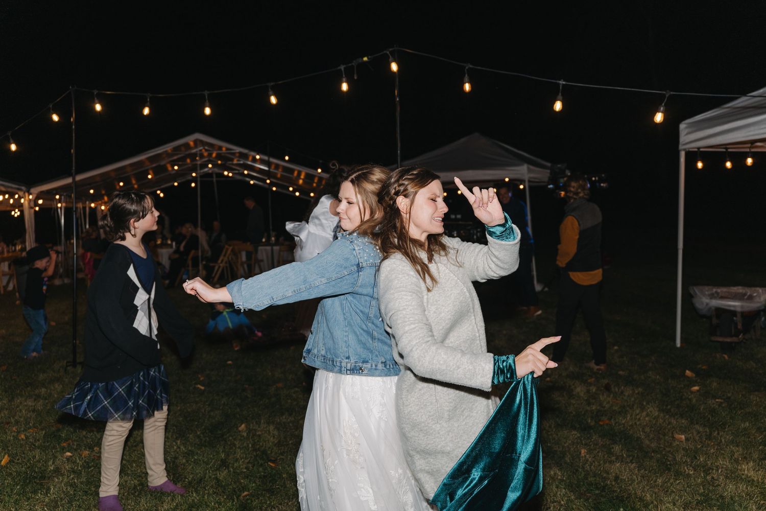 People dancing under string lights at an outdoor nighttime celebration in casual and formal attire.
