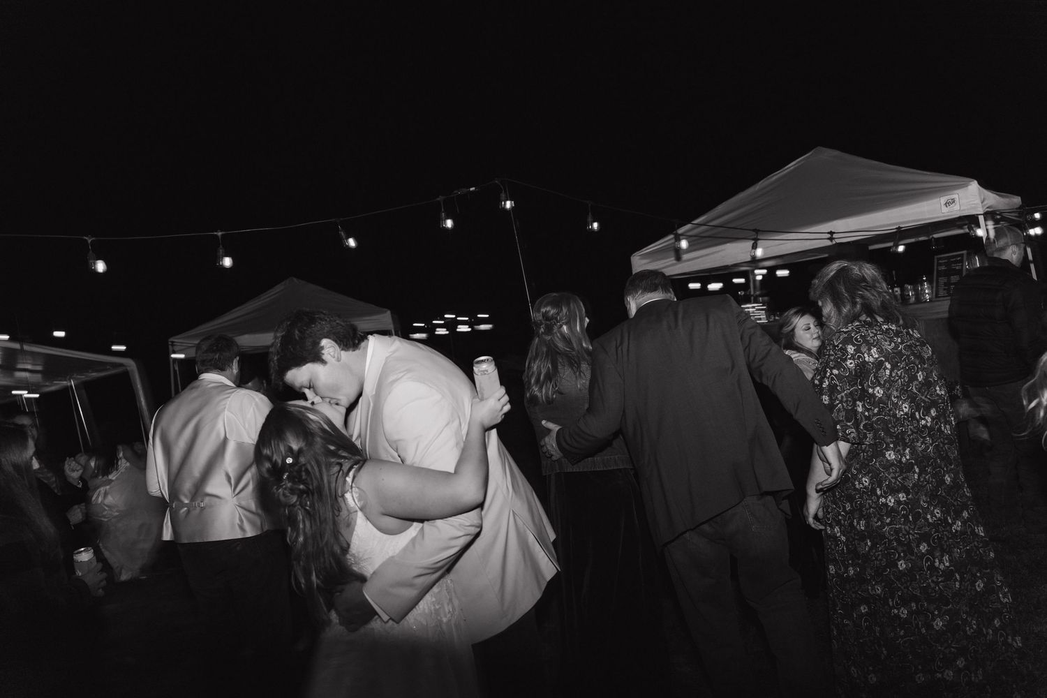 People dancing and mingling at an outdoor evening event under a tent in black and white photography.