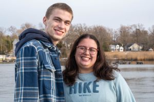 A couple poses together by a waterfront with boats and docks visible behind them.