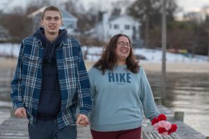 A happy couple laughs together while walking along a waterfront dock in winter.