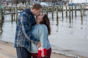 A couple shares an intimate moment by a marina with boats and docks in the background.