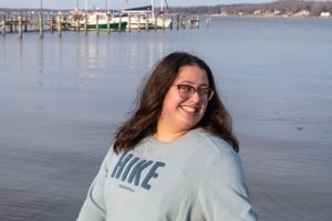 Person wearing a blue Nike sweatshirt smiles while standing by a marina waterfront.
