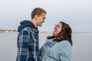 A couple gazes at each other while standing near a waterfront on a cloudy day.