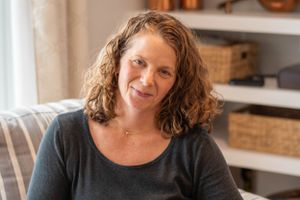 Person with curly hair sits on a couch with built-in shelving and storage baskets in background.