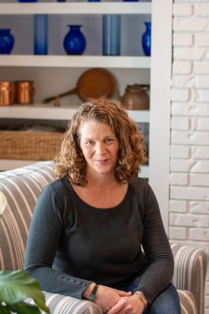 Person sits on couch with blue vases and copper decor displayed on white shelves behind.
