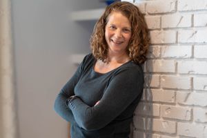 Person in black sweater poses against white brick wall with built-in shelving.