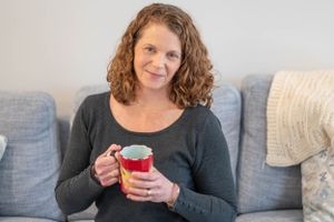 Someone holding a red mug while relaxing on a gray couch with throw pillows.