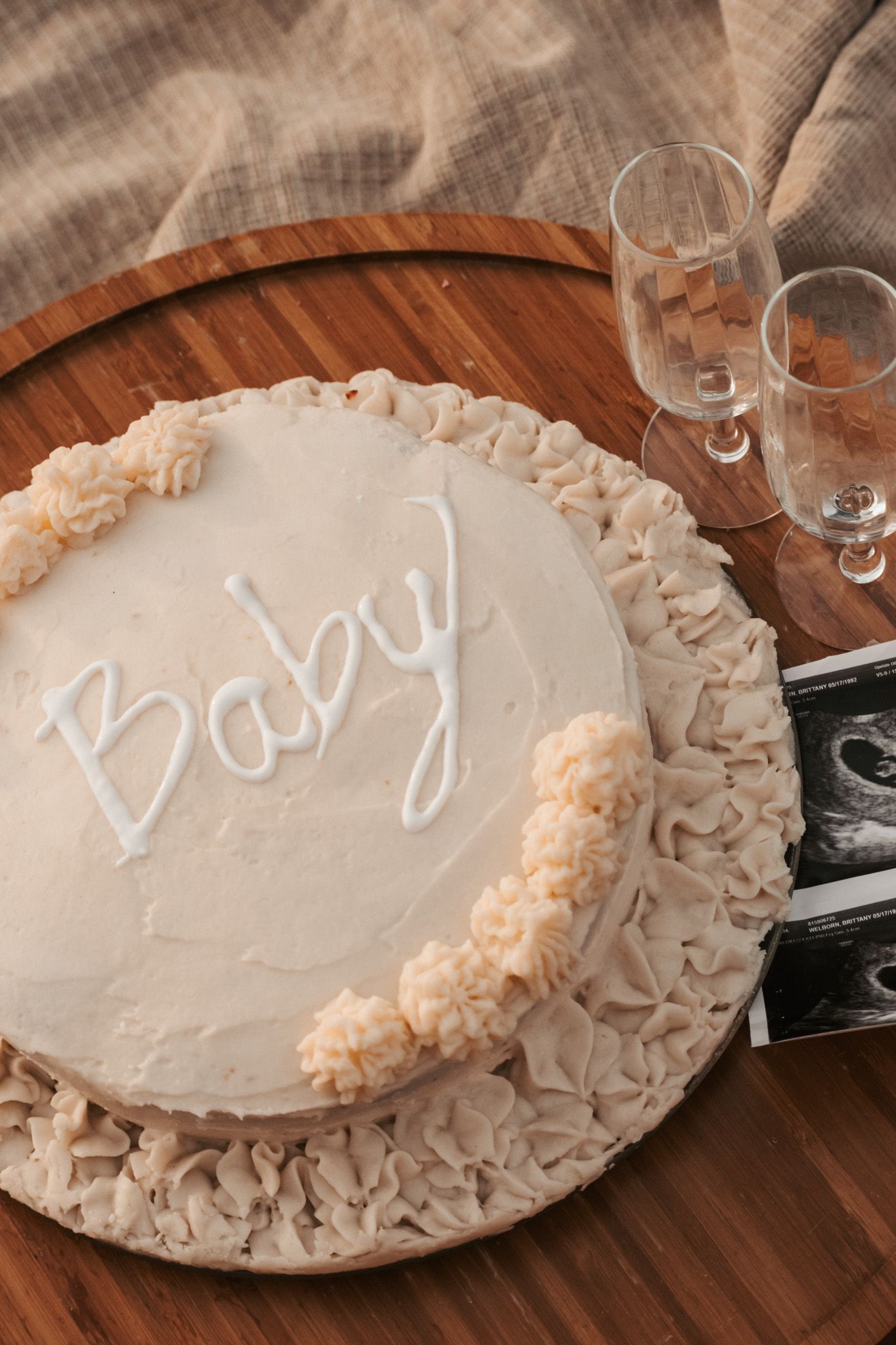 Baby gender reveal cake with ultrasound photo and champagne glasses on wooden tray.