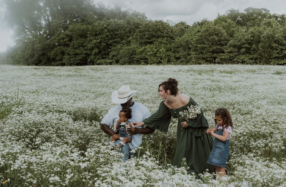 Family posing together in a blooming white wildflower field with lush green trees in the background.