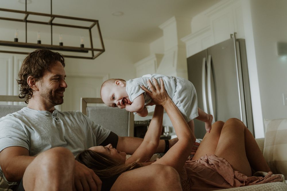 Happy family with parents and baby playing together on a couch in a bright, cozy living room.