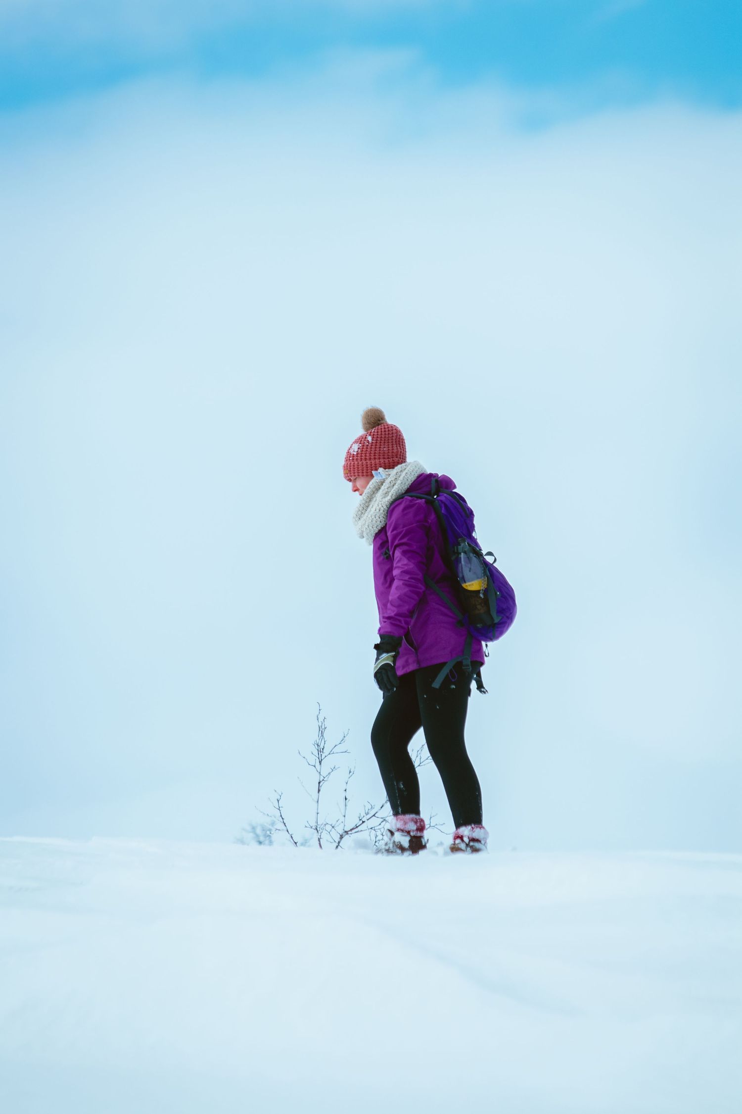 Person med ryggsäck och röd mössa står i ett snöigt landskap