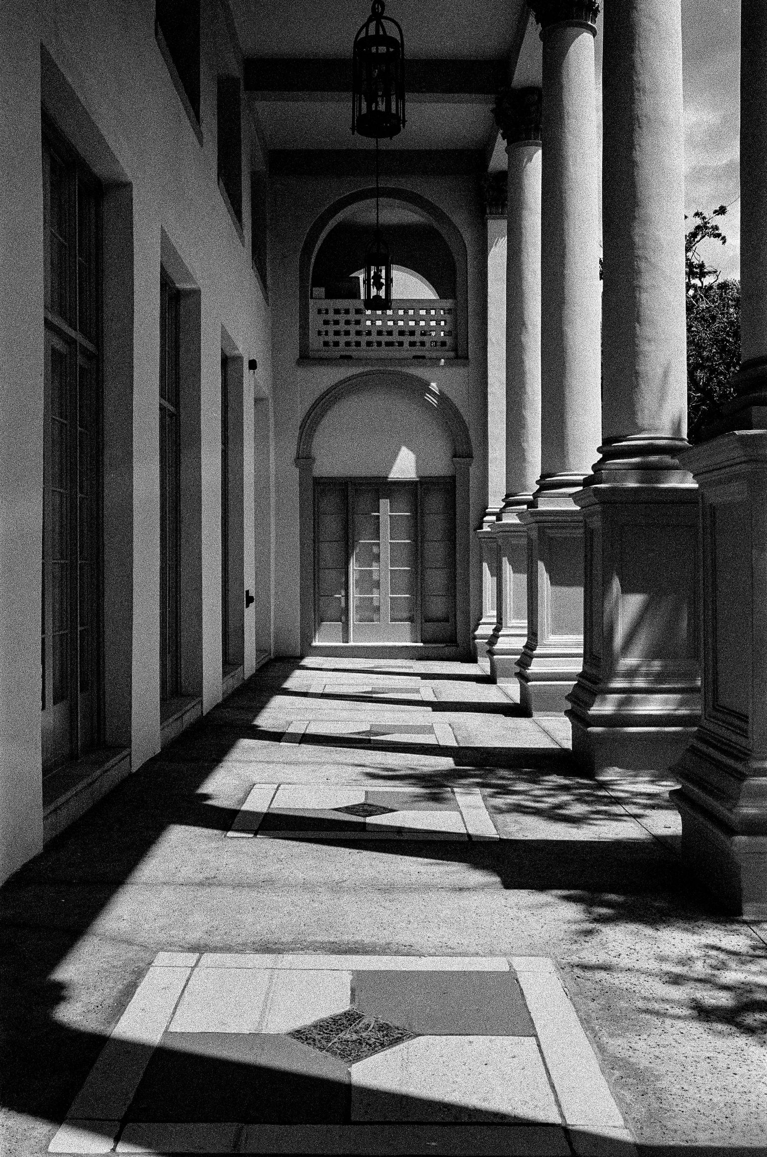 Dramatic shadows cast across a classical colonnade walkway with arched doorway.