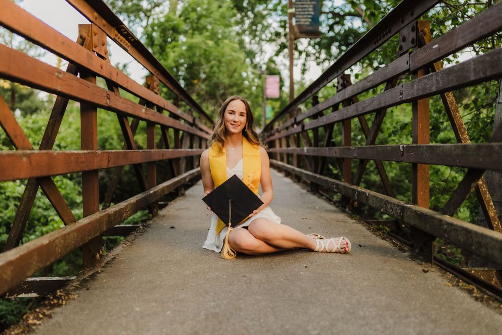 Graduate poses on wooden bridge with dramatic leading lines and natural framing.