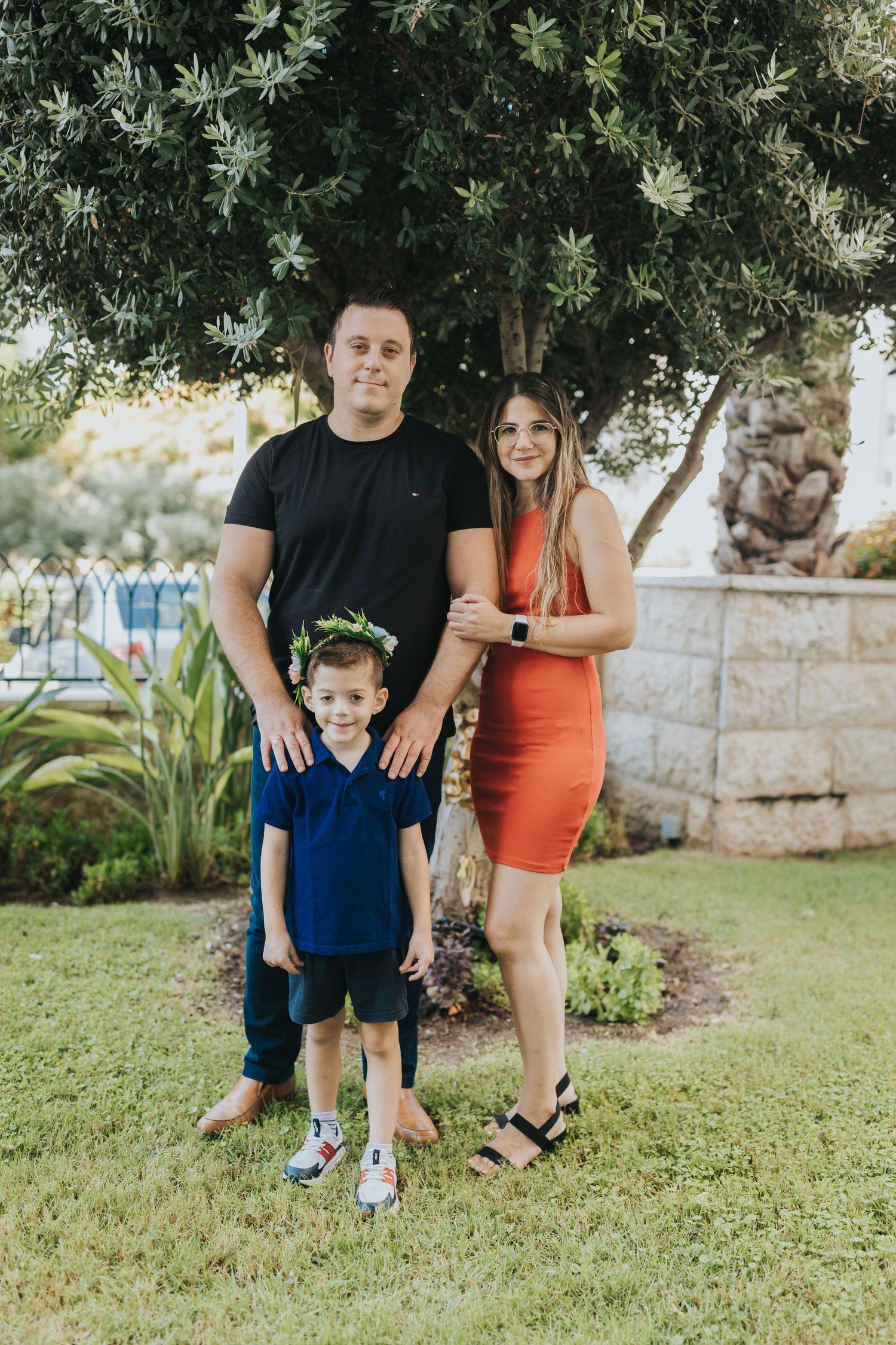 Family portrait outdoors with garden and stone wall backdrop.