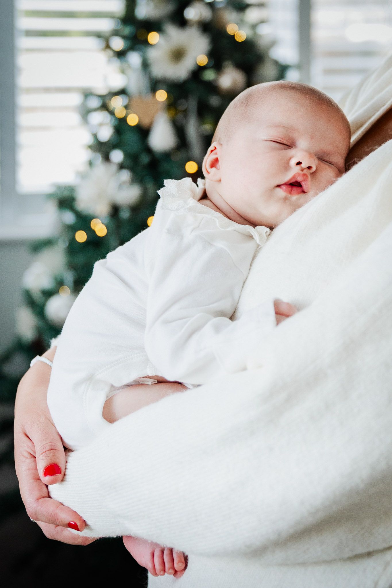 A newborn baby sleeps on her mother's chest in front of the Christmas tree. Bristol newborn photographer