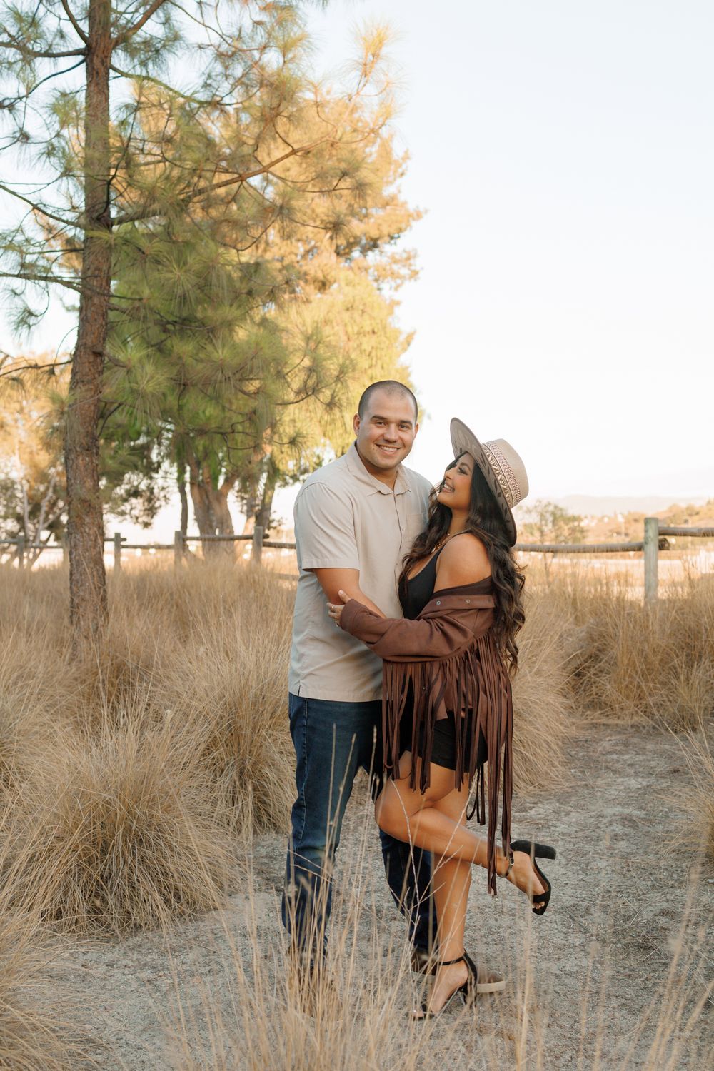 A couple embraces in a rustic outdoor setting with golden trees in the background.