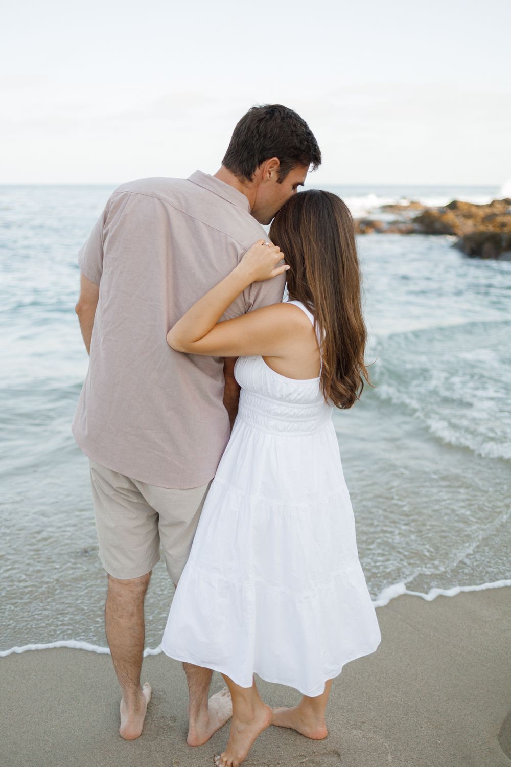 A couple shares an intimate moment on a rocky beach at sunset.