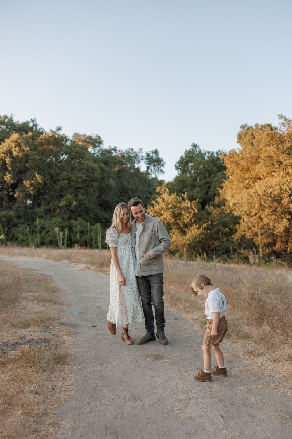 A family stands together on a dirt path surrounded by golden autumn trees at sunset.
