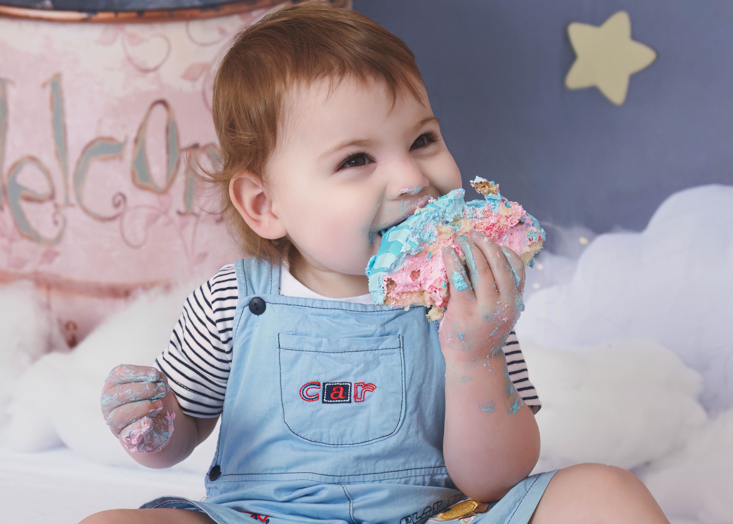 Little blonde boy eating a pink and blue cake during a cake smash session