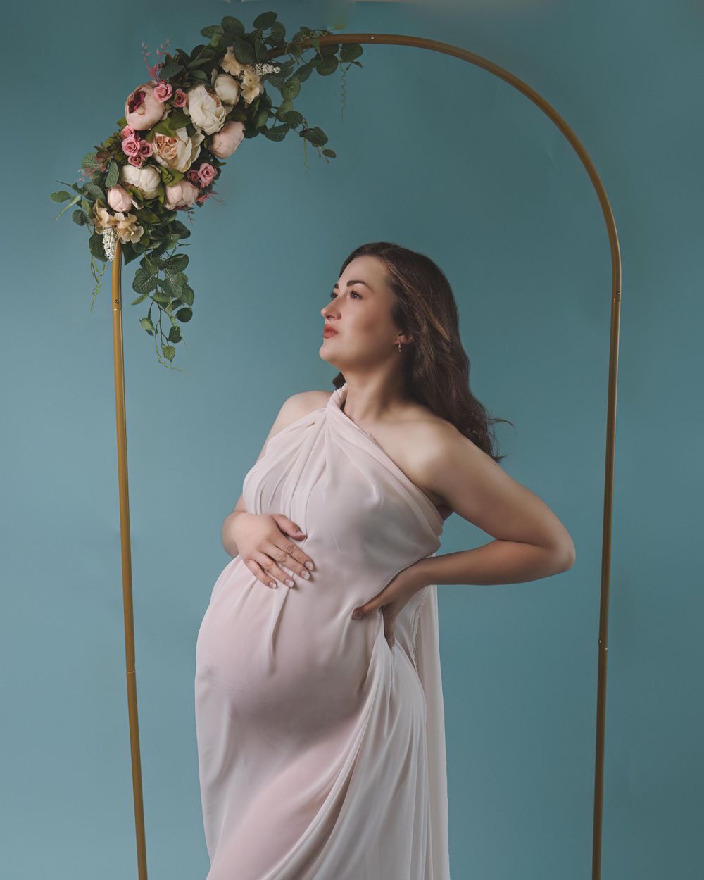 Maternity portrait of pregnant woman draped in white chiffon in art nouveau style.