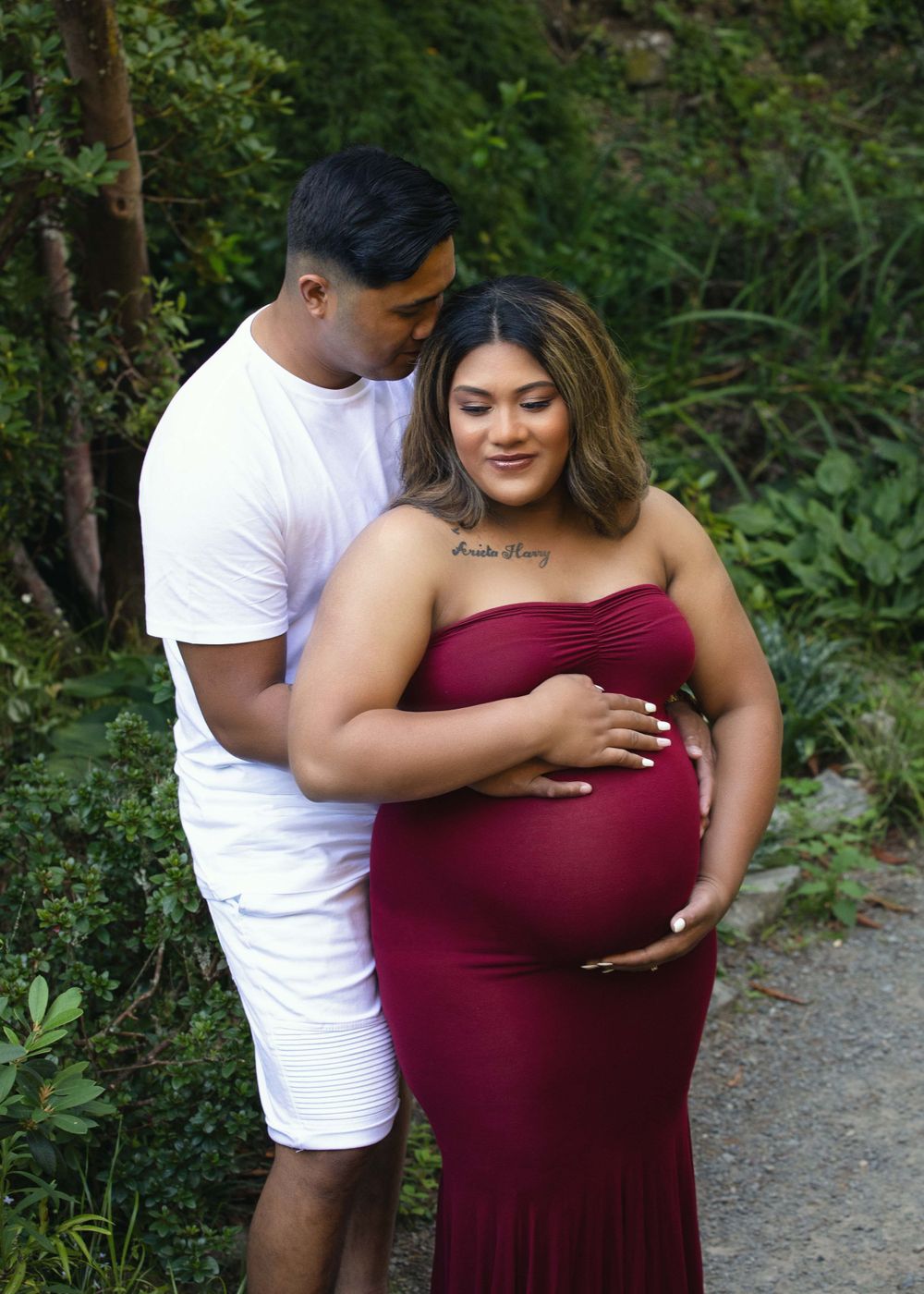 Couple's maternity portrait with husband whispering in pregnant woman's ear in the Wellington Botanical Gardens.