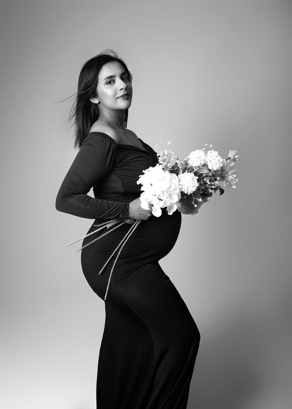Black and white portrait of pregnant woman holding flowers taken from the side.