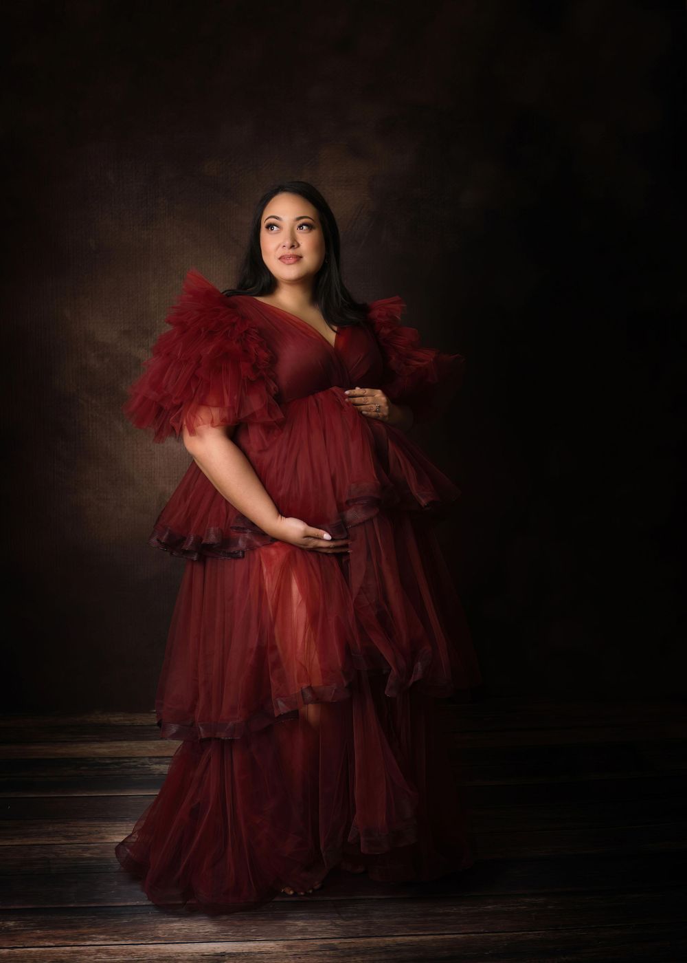Maternity portrait in the studio of a pregnant woman in red tulle dress.